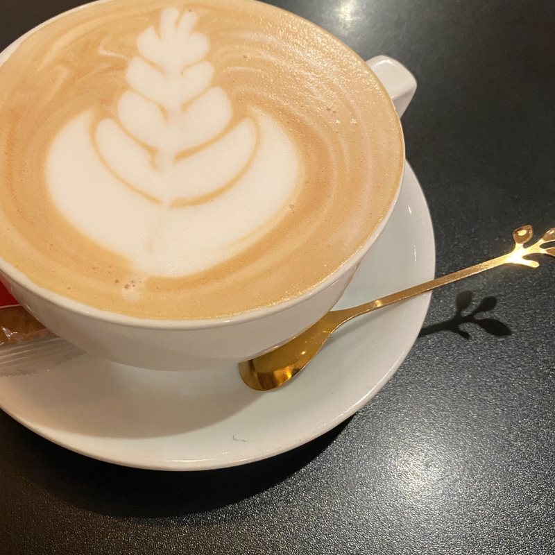 A latte with leaf latte art on a dark cafe table
